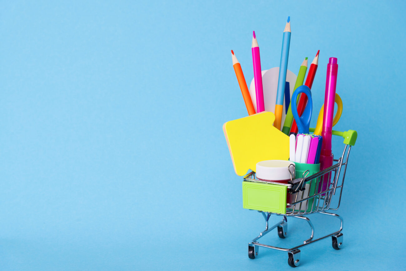 Bright Stationery Objects In A Mini Supermarket Trolley On A Blue Background. Back To School Concept
