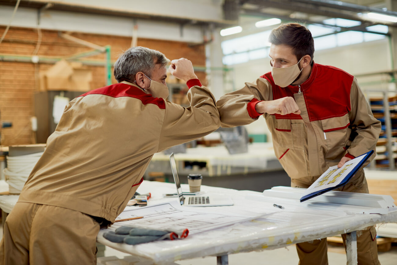 Happy Carpenters Elbow Bumping While Working In A Workshop Durin